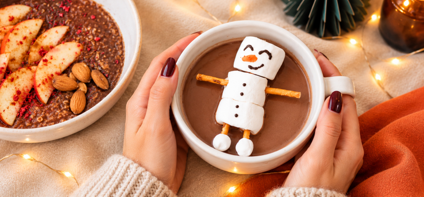Mâini de femeie țin o cană de cacao cu un om de zăpadă din marshmallow